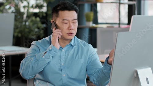 In a bright, modern office, a professional man speaks on the phone while focused on his computer screen. The atmosphere is calm and the workspace is well organized, enhancing productivity.