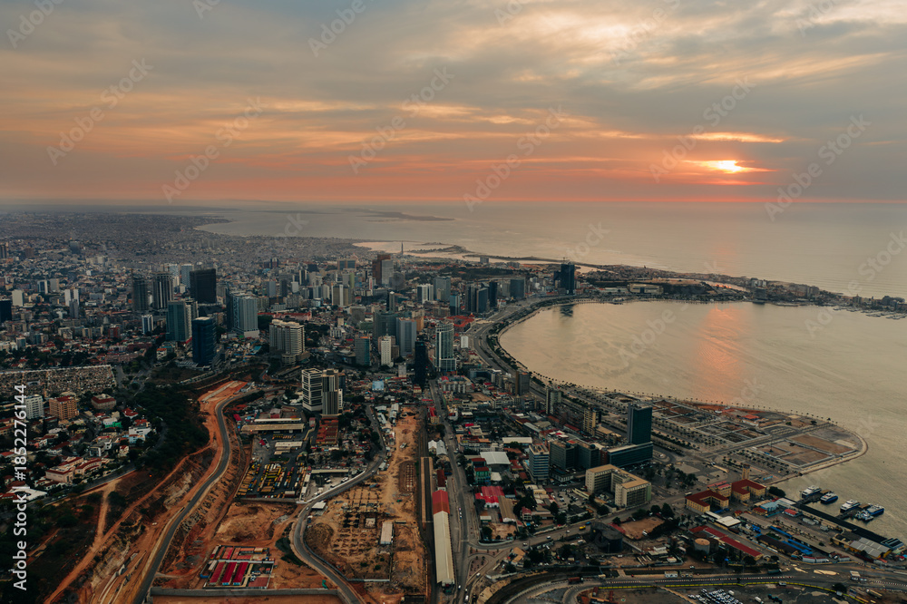 Naklejka premium Wide aerial view of Luanda skyline at sunset, vibrant African coastal city meeting the Atlantic Ocean, Angola
