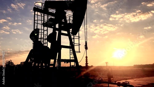 Oil Pump Jack Operates on Beautiful Sunset at Oil Field in Industrial Area. Crude pump jack working on sunrise in oil field. Oil drill rig, drilling derrick in oilfield. Crude petroleum industry. 