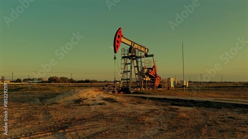 Oil Pump Jack Operates on Beautiful Sunset at Oil Field in Industrial Area. Crude pump jack working on sunrise in oil field. Oil drill rig, drilling derrick in oilfield. Crude petroleum industry. 
