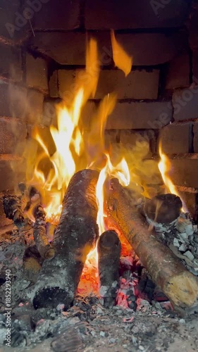 Close-up view of burning firewood in a traditional fireplace with glowing embers and warm flames. Cozy indoor atmosphere creating a sense of comfort, romance, relaxation, and slow living.