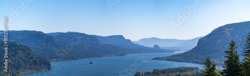 A scenic panorama view of the Columbia River Gorge in Portland Oregon with blue sky and lush green trees along the water and mountains.