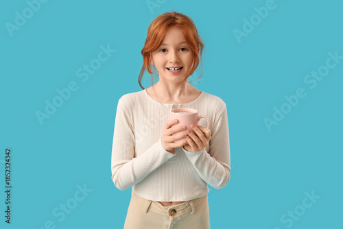 Photos Teenage redhead girl with cup of sweet cocoa on blue background