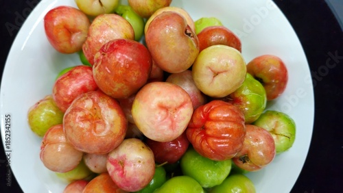 Tableau sur toile Close-up of fresh acerola cherries arranged on a white plate against a dark background