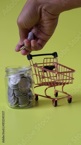 Hands putting coins into a jar next to a shopping trolley
