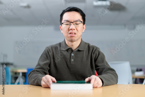 Foto A Chinese student sits at a desk with a book, showing a reluctant or unmotivated frown