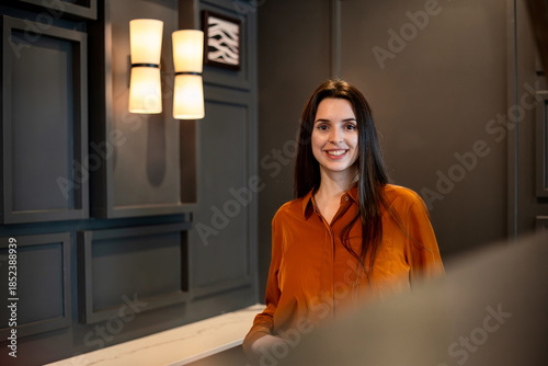 Smiling woman posing confidently in a modern interior with a dark wall, creating a relaxed and friendly portrait in a contemporary casual setting.