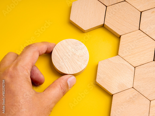 Concept of mismatch and problem solving with hand holding a round wooden piece not fitting into hexagon space. Symbolizes difference, challenge, creativity, unique thinking, and solution development.