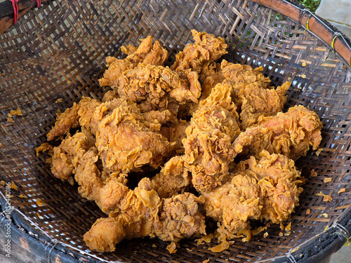 Crispy golden fried chicken pieces drained in a traditional woven basket after deep frying. Street food