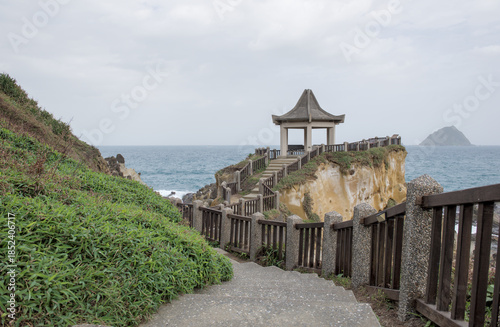 Traditional Chinese pavilion and concrete pathway along the coastal cliffs at Heping Island Park with Keelung Islet in the distance, Taiwan.