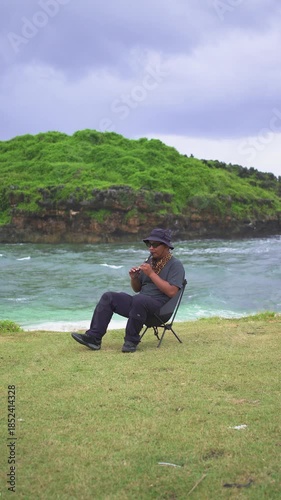 A male musician plays a tin whistle in nature with a beautiful ocean and small island in the background. A tin whistle player shows off his skills on a pristine and clean tropical beach.