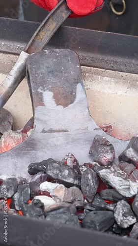 Blacksmiths traditional metalworking techniques using heated tools in axe making setting.