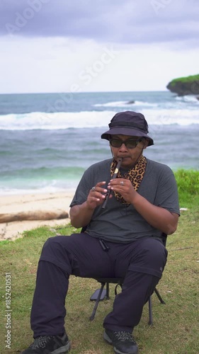 A male musician plays a tin whistle in nature with a beautiful ocean and small island in the background. A tin whistle player shows off his skills on a pristine and clean tropical beach.