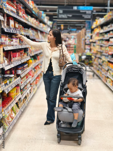 Mother grocery shopping with baby in supermarket aisle