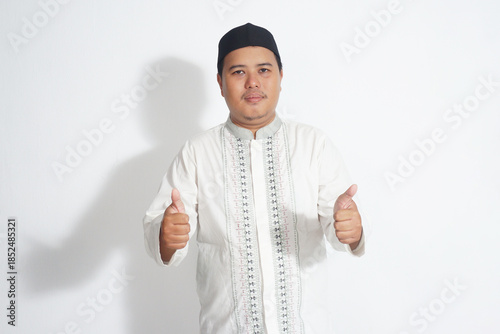 an Indonesian Muslim man wearing a black peci and a white koko shirt is giving two thumbs up on a plain white background        