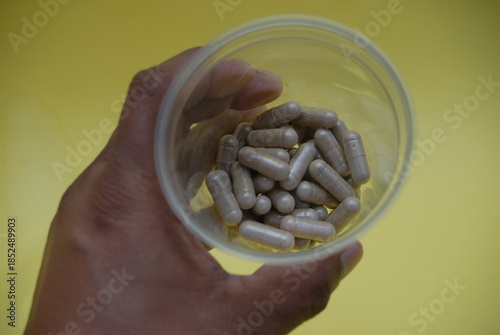Close up of hand holding transparent jar with brown medical capsules
