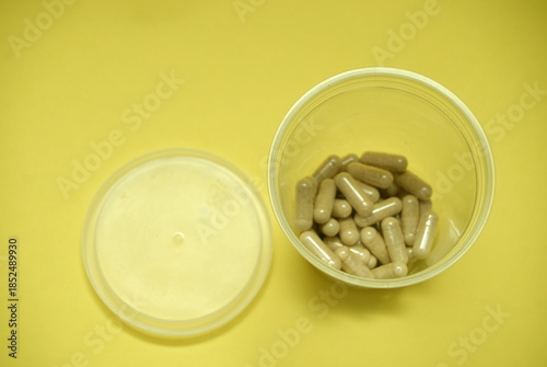 Open container with natural supplement capsules on yellow background