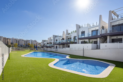 Sunny residential complex with curved swimming pool and artificial grass landscaping