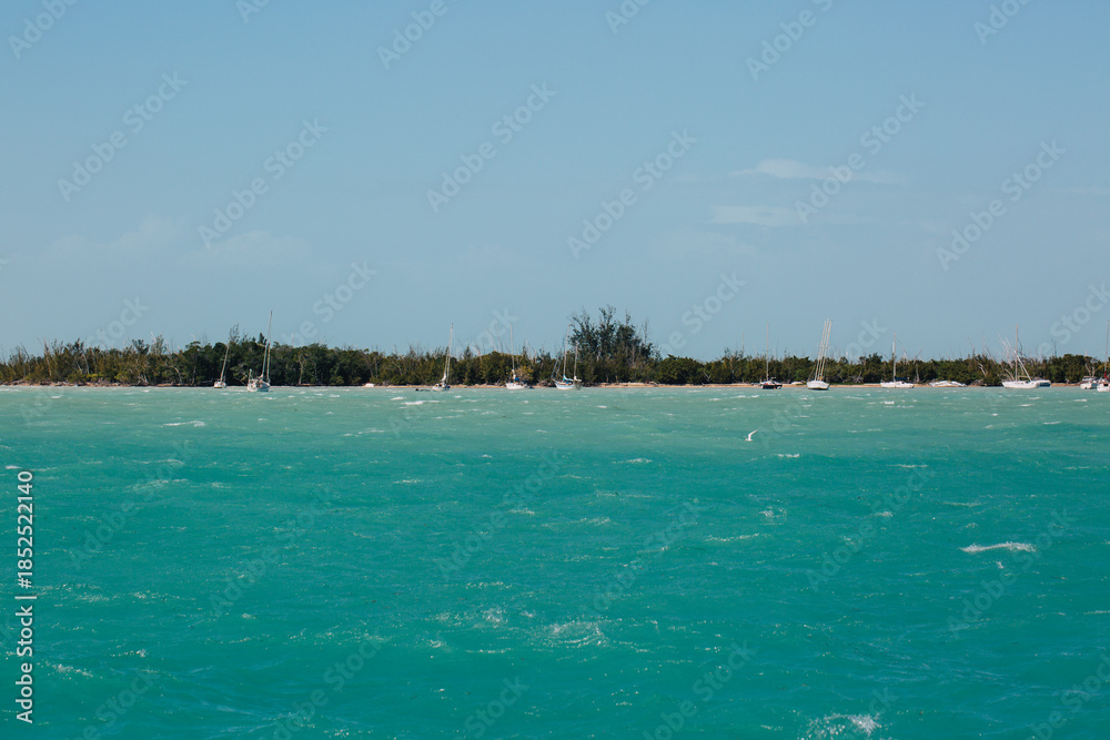 Fototapeta premium Turquoise Coastal Waters with Sailboats Near Tropical Shoreline