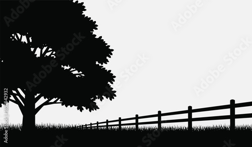 A striking silhouette of a large tree and a rustic wooden fence stretching into the distance creating a peaceful scene