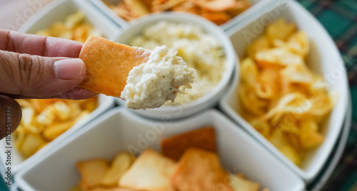 Fotografie Hand dipping cracker into creamy artichoke dip
