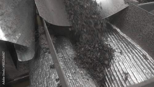 Shredded rubber disappears between rotating grooved metal rollers. Industrial recycling equipment performs compression and transfer stage