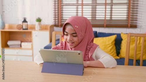 Asian Muslim girl using a digital tablet in cozy living room at home.        