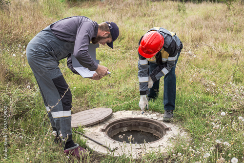 Workers in overalls peer into an open manhole, inspecting faulty water pipes and water meters
