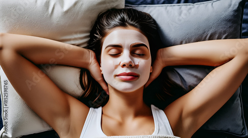 Woman reclining on soft bed surrounded by pillows with soothing facial mask