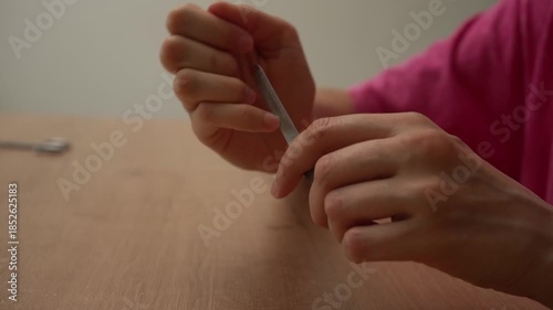 Detailed close-up view of a person's hands as they meticulously file their fingernails with a metal nail file, focusing on personal hygiene, self-care, and nail grooming at home