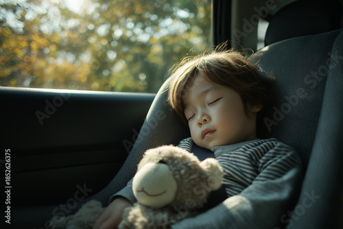 Cute little child sleeping in car safety seat holding stuffed toy during road trip