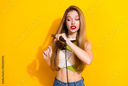 Tableau sur toile Young woman straightening her long blonde hair with a flat iron against a vibran