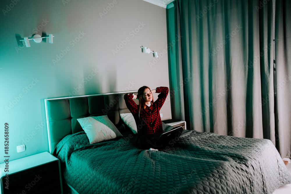 Naklejka premium Young woman studying on bed with laptop in bedroom during evening