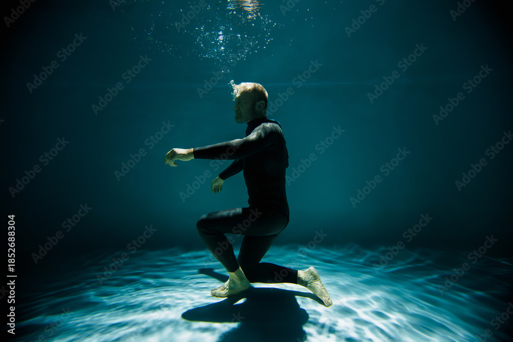 Fototapeta premium Free diver in wetsuit holding breath while training underwater in pool