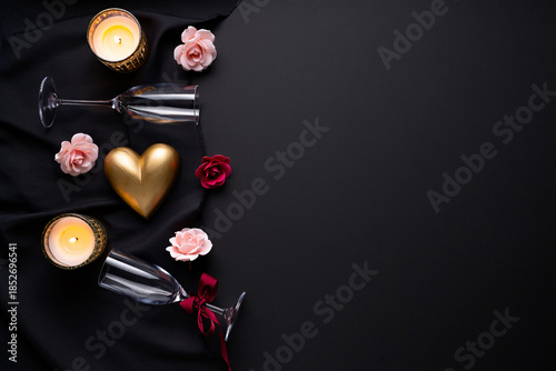 Romantic dark background flat lay with golden heart champagne flutes and lit candles