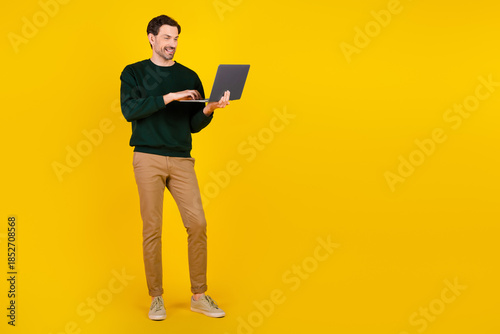 Cuadro en lienzo Young man with laptop standing against a bright yellow background wearing green