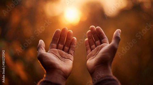 Human hands open with palms up in silhouette against a golden, warm sunset or sunrise sky, symbolizing hope, spirituality, and prayer in nature