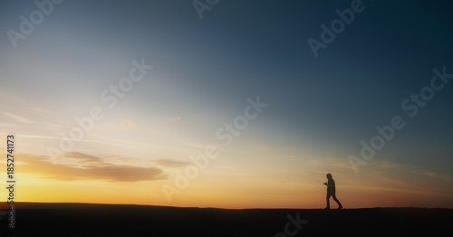 Fotografie Silhouette of a person walking at sunset with a colorful sky and horizon, evokin
