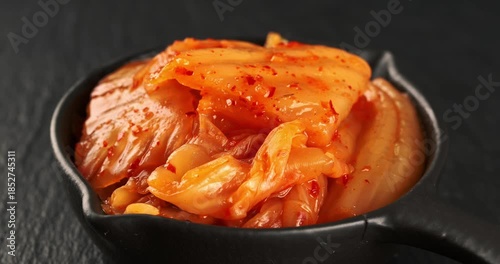 Bowl with korean traditional cabbage kimchi on dark background. Hot fermented napa cabbage. Close-up footage on the rotating table.
