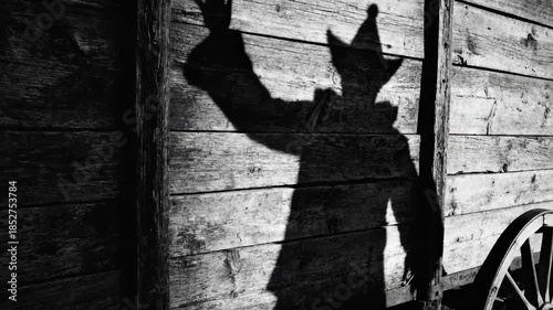Circus clown casting elongated shadow on wooden wagon panels. Performer in hat extends arm in dramatic pose. Traditional big top silhouette show for entertainment.