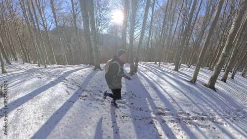 Monte Lema, Varese, Italy: A hiker man black dressed runs in the winter wood on the snow