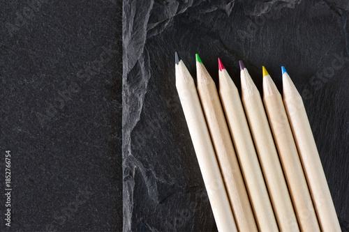 Group of colored wooden pencils lying on f two different grey stone texturs with varying degrees of roughness and layering.