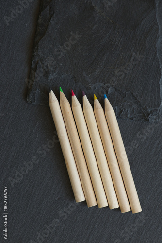 Group of colored wooden pencils lying on f two different grey stone texturs with varying degrees of roughness and layering.