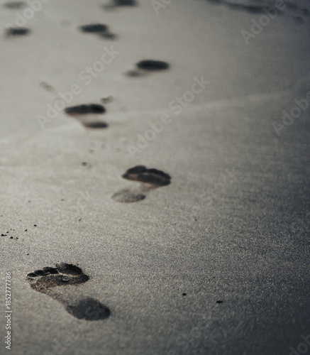 A black volcanic sand on a beach closeup with a person footprints.