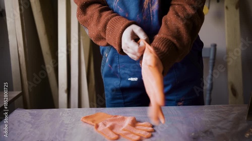 Close up of female carpenter putting on orange protective work gloves in woodworking workshop