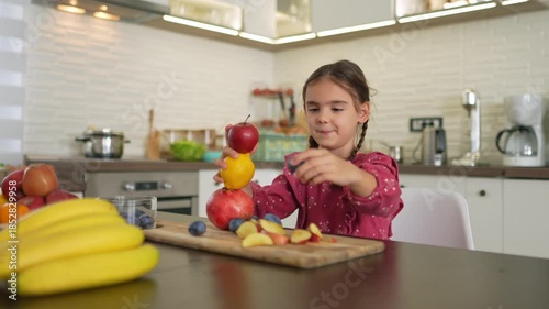 Girl playing in the kitchen happily building a fruit tower