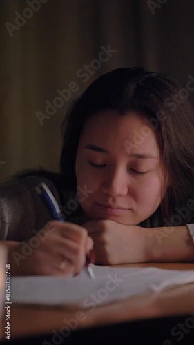 A young woman sitting at a table in her cozy home during the evening, thoughtfully writing in a notebook. Soft warm lighting creates an intimate and reflective atmosphere. Perfect for concepts of crea