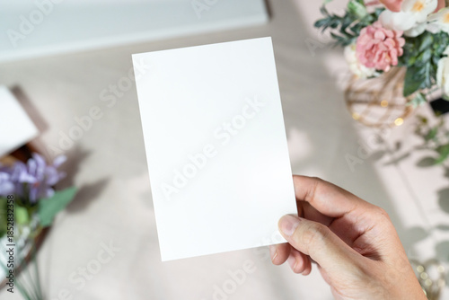 Quadro em tela Mockup of a blank white card held by hand with soft blurred flowers, perfect for wedding or Valentine’s greeting design, with clipping path