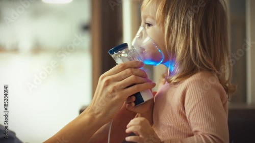 Caring mother assists her child with aerosol inhalation treatment using nebulizer, carefully holding mask to their face. As educator and mentor, she guides the process for the child's asthma relief