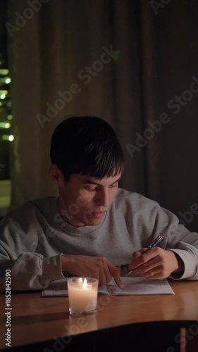 A young man sitting at a table in his cozy home during the evening, thoughtfully writing in a notebook. Soft warm lighting creates an intimate and reflective atmosphere. Perfect for concepts of creati